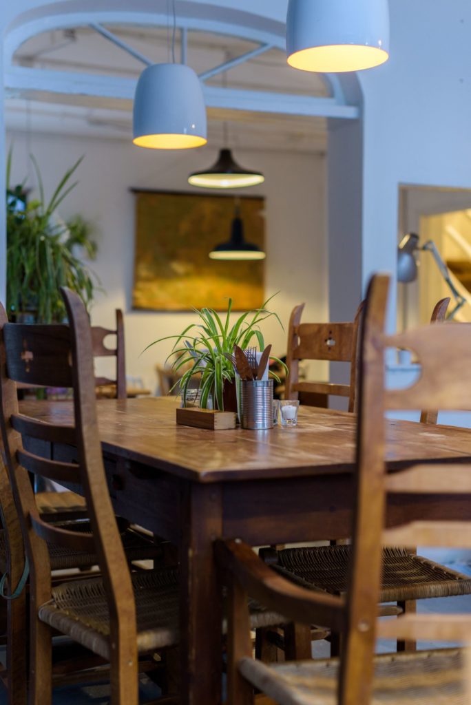 Cozy dining area featuring a wooden table surrounded by chairs, adorned with a small plant centerpiece, cutlery holder, and salt shaker, enhanced by stylish pendant lighting. Ideal for inviting meals and gatherings.