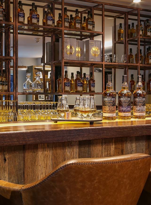Interior view of a stylish whiskey bar showcasing an array of premium whiskey bottles on shelves, with elegant glassware displayed on a wooden counter. The warm lighting highlights the rich textures of the decor, creating an inviting atmosphere for whiskey enthusiasts.